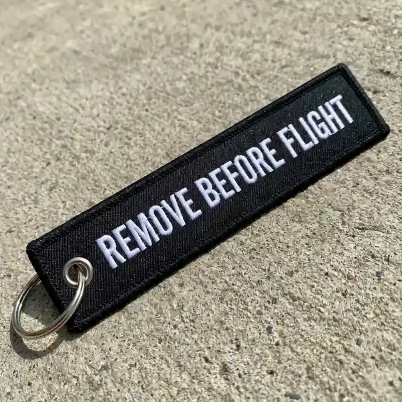 Fabric 'Remove Before Flight' style keychain with embroidered text.